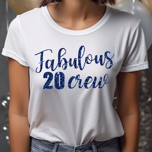 以下が含まれることがあります： 「Fabulous 20 Crew」という青いグリッターの文字が書かれた白いTシャツです。