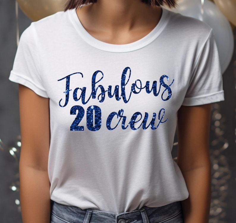 以下が含まれることがあります： 「Fabulous 20 Crew」という青いグリッターの文字が書かれた白いTシャツです。