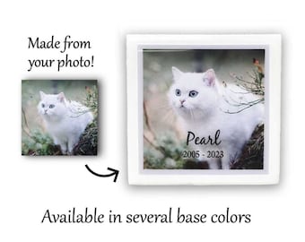May include: White ceramic pet memorial with a photo of a white cat with blue eyes. The cat is sitting in a forest setting. The text "Pearl 2005-2023" is printed below the photo.