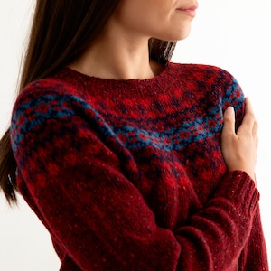 Model wearing Red Croft Yoke pattern fair isle jumper. Pattern with blue and brighter scarlet red.