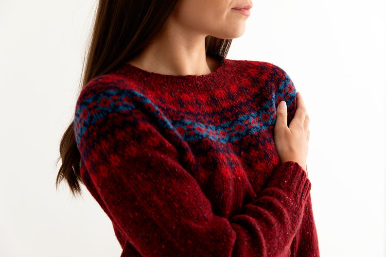 Model wearing Red Croft Yoke pattern fair isle jumper. Pattern with blue and brighter scarlet red.