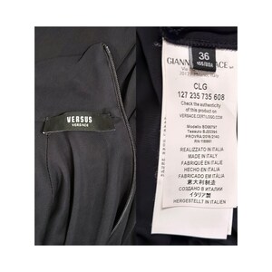 May include: Black dress with a zipper closure and a white label with the text "VERSUS VERSACE" and a white tag with the text "GIANNI 155/80A ACE" and "CLG 127 235 735 608" and "Check the authenticity of this product on VERSACE CERTILOGO.COM" and "Modello BD00797 Tessuto BJ20394 PROVRA 2016/2140 RN 118881" and "REALIZZATO IN ITALIA MADE IN ITALY FABRIQUE EN ITALIE HECHO EN ITALIA FABRICADO EM IT&Aacute;LIA 意大利制造 СОЗДАНО В ИТАЛИИ イタリア製 HERGESTELLT IN ITALIEN"