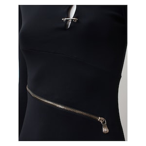 May include: Black long-sleeved dress with a silver zipper detail and a silver safety pin closure at the neckline.