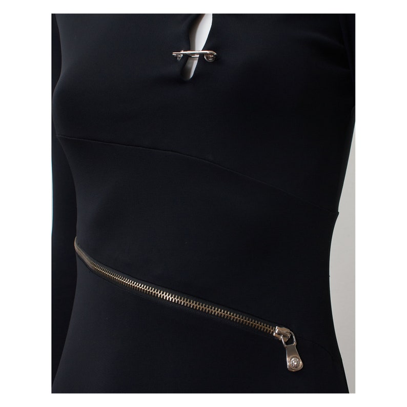 May include: Black long-sleeved dress with a silver zipper detail and a silver safety pin closure at the neckline.