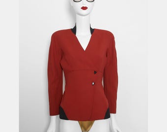 May include: A red long-sleeve blazer with a V-neck and black accents. The blazer features two black buttons and is displayed on a mannequin wearing sunglasses and a black hat. The blazer has a tailored fit.
