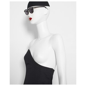 May include: A mannequin wearing black sunglasses with black frames, a black beanie, and a black strapless top. The mannequin has red lipstick and is set against a white background.