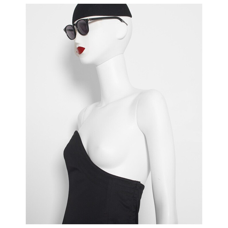 May include: A mannequin wearing black sunglasses with black frames, a black beanie, and a black strapless top. The mannequin has red lipstick and is set against a white background.