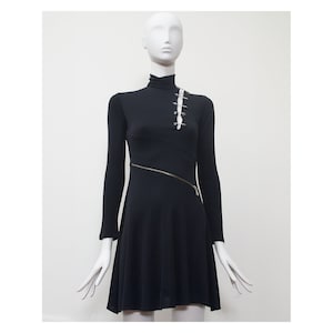 May include: A black long-sleeved dress with a mock neck and a diagonal zipper. The dress has a fitted bodice and a flared skirt. There are safety pins on the bodice.
