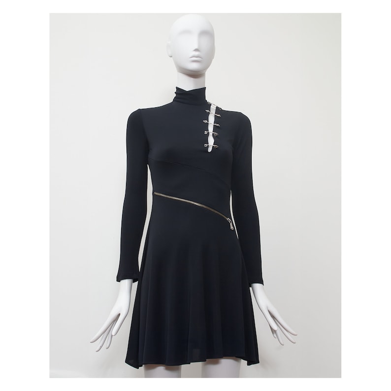 May include: A black long-sleeved dress with a mock neck and a diagonal zipper. The dress has a fitted bodice and a flared skirt. There are safety pins on the bodice.