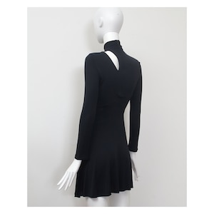 May include: Black long-sleeved dress with a mock neck and a keyhole cutout at the back of the neck. The dress has a fitted bodice and a flared skirt.