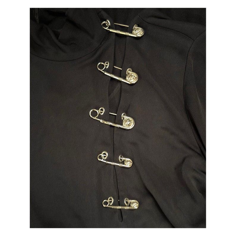 May include: Black long-sleeved shirt with a row of silver safety pins with decorative heads down the front.
