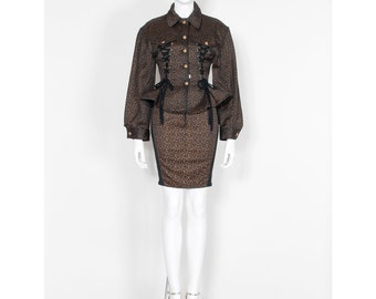 Könnte beinhalten: Ein schwarzer und brauner gemusterter Rockanzug mit einem Schnürkorsett und einem figurbetonten Rock. Die Jacke hat lange Ärmel und einen Kragen.