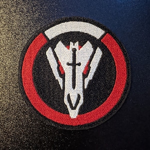 May include: A red and white embroidered patch with a skull and crossbones design. The skull is white with a black outline and the crossbones are white. The patch is circular and has a red border.