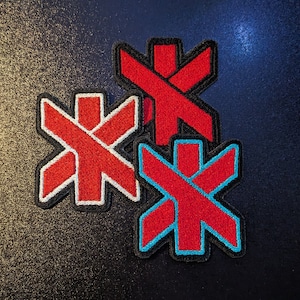 Puede incluir: Tres parches bordados de color rojo y blanco en forma de estrella con una cruz en su interior. Los parches están sobre un fondo gris oscuro.