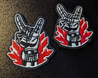 May include: Two black and white embroidered patches with a skeleton hand making the rock and roll hand gesture. The hand is surrounded by red flames.