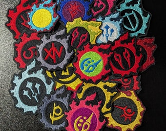 May include: A collection of colorful, embroidered patches with various symbols and designs. Each patch has a unique shape and features a different color scheme, including red, blue, yellow, and purple. The patches appear to be related to a video game or fantasy theme.