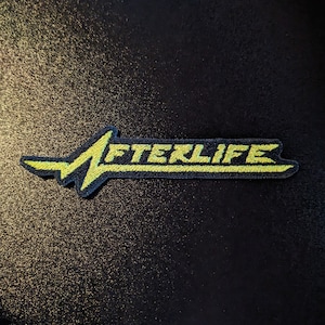 Puede incluir: Un parche bordado negro y amarillo con la palabra "AFTERLIFE" en una fuente estilizada.
