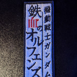 May include: Blue and white embroidered patch with Japanese text that reads "機動戦士ガンダム" and "鉄のオルフェンズ".
