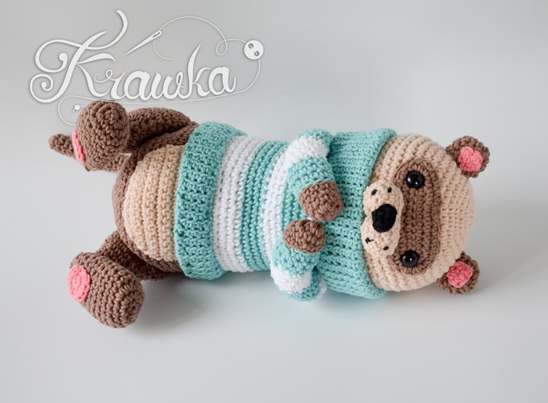 May include: A crocheted stuffed animal in the shape of a bear wearing a blue and white striped sweater. The bear has brown fur, a black nose, and pink ears.