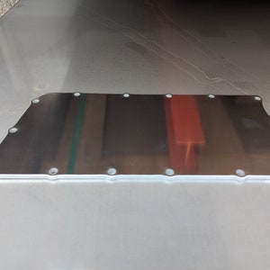 May include: A silver metal plate with a smooth, reflective surface. The plate has a rectangular shape with rounded corners and multiple small holes around the edges.