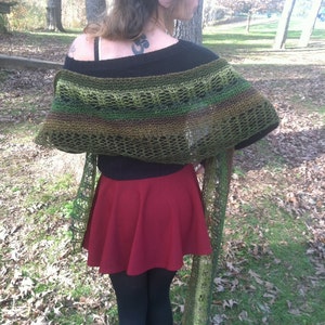 May include: A black off-the-shoulder sweater paired with a red skater skirt and black leggings. A green and brown crocheted shawl is draped over the shoulders. The outfit is worn outdoors in a park setting.