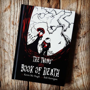 May include: A hardback book titled "The Twins' Little Book of Death" with a black cover and a gothic illustration. The illustration features a woman in a long black dress and a boy in a red scarf, with a tree and a graveyard in the background.