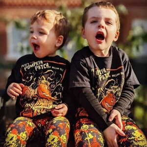 May include: Two young boys wearing black and orange shirts with a pumpkin patch theme. The shirts feature the text "Pete's Pumpkin Patch, Hollow Hill". The boys are wearing matching black and orange pants with a pumpkin and leaf pattern.