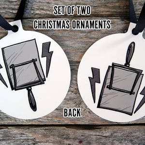 May include: Set of two white Christmas ornaments featuring a black and gray illustration of a vintage hand mirror with lightning bolts. The back of the ornament says "Back".