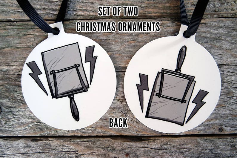 May include: Set of two white Christmas ornaments featuring a black and gray illustration of a vintage hand mirror with lightning bolts. The back of the ornament says "Back".