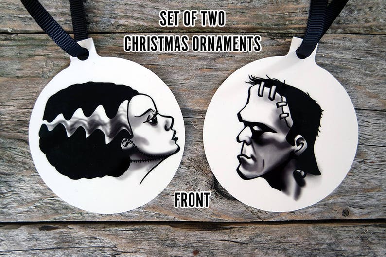 May include: Set of two round Christmas ornaments featuring black and white illustrations of Frankenstein's monster and his bride. The ornaments are white with black outlines and are labeled "Set of Two Christmas Ornaments" and "Front".