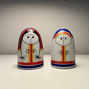 Puede incluir: Un par de saleros y pimenteros de cerámica con un diseño nativo americano. Los saleros son blancos con acentos rojos, azules y amarillos. Las caras son simples con ojos negros y una boca negra.