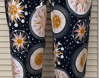 May include: Dark navy blue pajama pants with a celestial sun and star pattern. The pants feature a drawstring waist and a repeating design of suns, moons, and stars in gold, white, and pink.