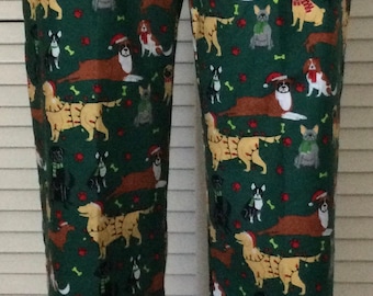 May include: Green pajama pants with a repeating pattern of various dog breeds wearing Santa hats and scarves. The pants have a drawstring waist and a relaxed fit, perfect for lounging. The dogs are in various poses.