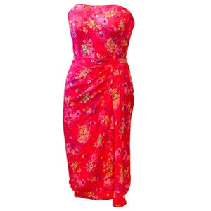 May include: A strapless, knee-length dress in a vibrant red hue, adorned with a delicate floral pattern in shades of pink, yellow, and orange. The dress features a draped design at the waist and a fitted silhouette.