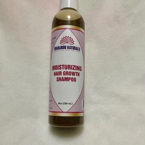 Pode incluir: Uma garrafa de plástico marrom de shampoo hidratante para o crescimento do cabelo com um rótulo branco. O rótulo tem um design de flor de lótus rosa e o texto "Marabou Naturals Established 2015" e "Shampoo hidratante para o crescimento do cabelo". A garrafa é de 8 oz (236 ml).