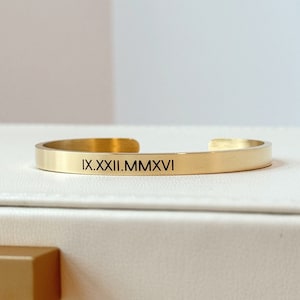 May include: A gold-toned bangle bracelet with the inscription "IX.XXII.MMXVI" engraved on the front.