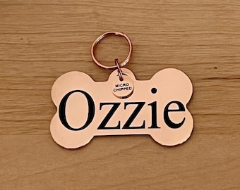 May include: A copper bone-shaped dog tag with the name "Ozzie" engraved in black lettering. A small round tag with the words "Micro Chipped" is attached to the ring.