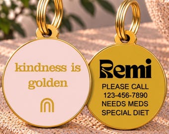 Op de afbeelding: Twee ronde goudkleurige metalen naamplaatjes voor huisdieren met splitringen. Eén plaatje heeft een lichtroze emaille voorzijde met de gouden tekst "kindness is golden" en een regenboogicoon. Het andere is goudkleurig metaal met zwarte tekst: "Remi", "PLEASE CALL 123-456-7890", "NEEDS MEDS", "SPECIAL DIET".