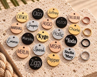 May include: A collection of circular metal pet ID tags in gold, silver, rose gold, and black finishes, each engraved with a unique name including Chewie, Ozzy, Joffrey, Tallulah, Marshall, Jasper, Hugo, Astor, Charlie, Emma, Murphy, Kygo, Halle, Yoda, Merlin, Spark, Misha, Stella May, Ziggy, and Pepper, accompanied by four metal split rings in matching metallic tones.