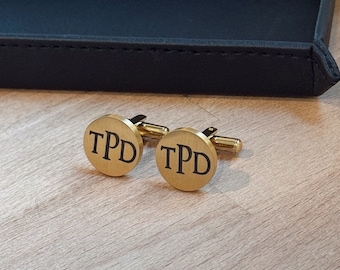 May include: A pair of gold-toned cufflinks with the initials "TPD" engraved in black.