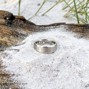 May include: A silver wedding band with a brushed finish and the inscription "XXV.MMXX" on the inside of the band.
