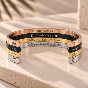 May include: A stack of four metal cuff bracelets in rose gold, black, gold, and silver tones. The bracelets feature engraved text including IV XII MMXXIII, GOOD VIBES, Oakley, Otto, Ocean, and she believed she could, so she did, plus icons.