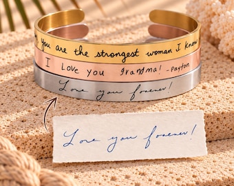 May include: Three stacked metal cuff bracelets in gold, rose gold, and silver tones. Each bracelet features custom black cursive engraving. The top reads, you are the strongest woman I know, the middle, I Love you Grandma! -Payton, and the bottom, Love you forever!