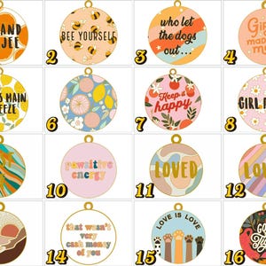 May include: A collection of sixteen circular metal charms featuring various colourful designs and text, including phrases like Bad and Boujee, Bee Yourself, Girl Power, Loved, and Love is Love, each with a small gold loop at the top for attachment.