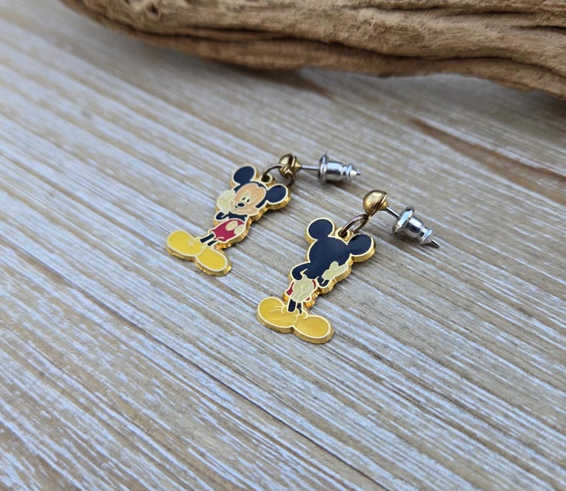 Puede incluir: Un par de pendientes de Mickey Mouse de tono dorado. Los pendientes presentan una imagen de dibujos animados de Mickey Mouse con pantalones cortos rojos y zapatos amarillos. Los pendientes est&aacute;n unidos a postes plateados.