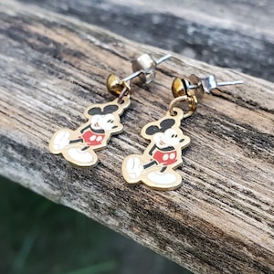 Puede incluir: Un par de pendientes de Mickey Mouse de color dorado. Los pendientes presentan una imagen de dibujos animados de Mickey Mouse con su caracter&iacute;stico pantal&oacute;n rojo y guantes blancos. Los pendientes est&aacute;n unidos a postes de color plateado.