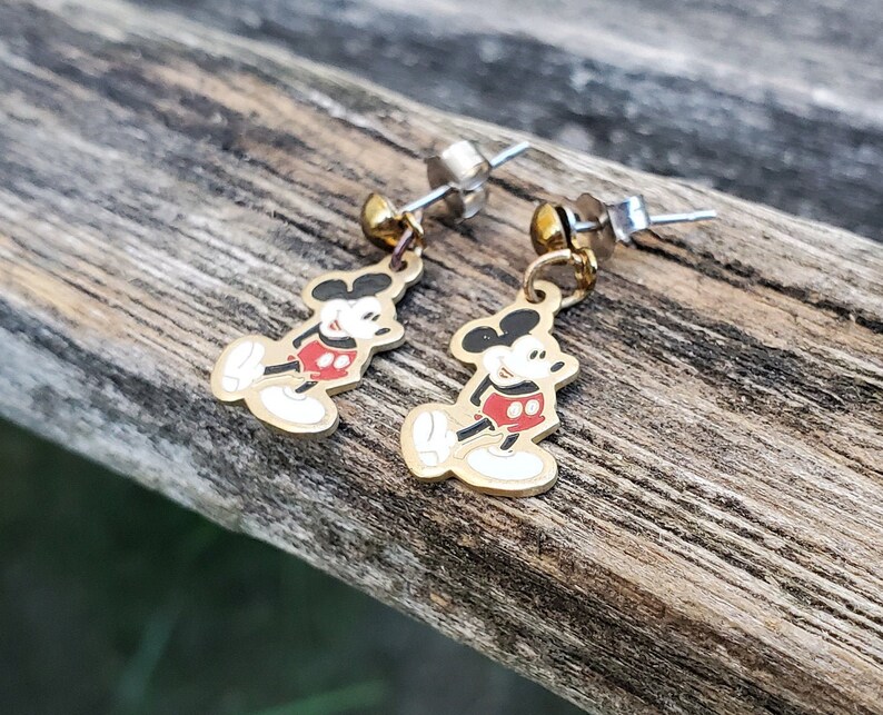 Puede incluir: Un par de pendientes de Mickey Mouse de color dorado. Los pendientes presentan una imagen de dibujos animados de Mickey Mouse con su caracter&iacute;stico pantal&oacute;n rojo y guantes blancos. Los pendientes est&aacute;n unidos a postes de color plateado.