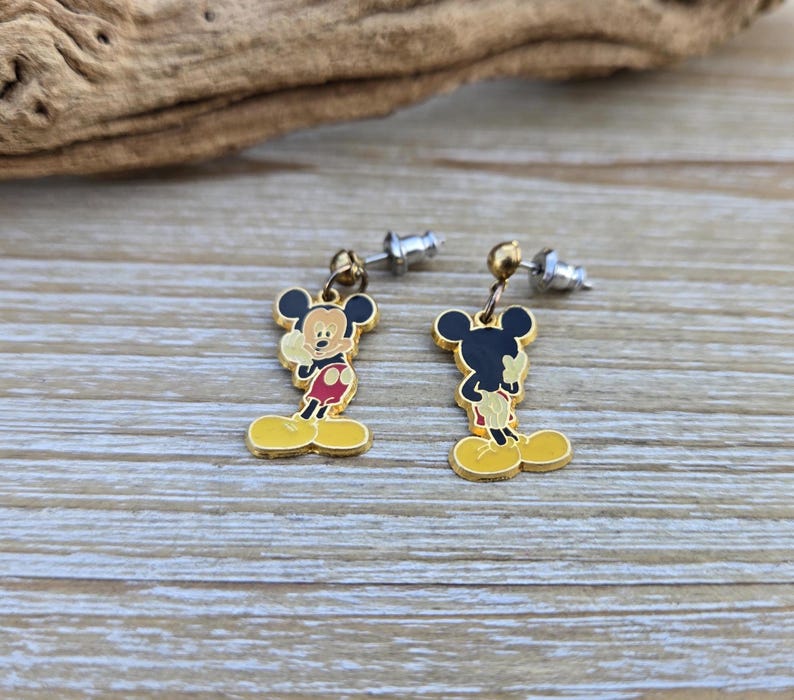 Puede incluir: Un par de pendientes de Mickey Mouse de tono dorado. Los pendientes presentan una imagen de dibujos animados de Mickey Mouse con ojos negros, pantalones cortos rojos y zapatos amarillos. Los pendientes est&aacute;n unidos a postes de tono plateado.