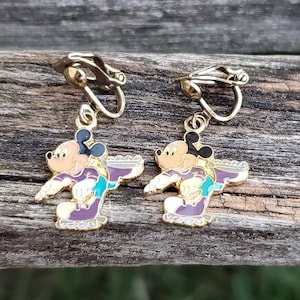 K&ouml;nnte beinhalten: Ein Paar goldfarbene Ohrclips mit einem Cartoon-Bild von Mickey Mouse beim Eislaufen. Die Ohrringe sind mit lila, t&uuml;rkis und schwarzem Email verziert.