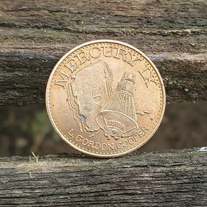May include: A gold-colored coin with the words "Mercury IX L Gordon Cooper" and an image of a space capsule.